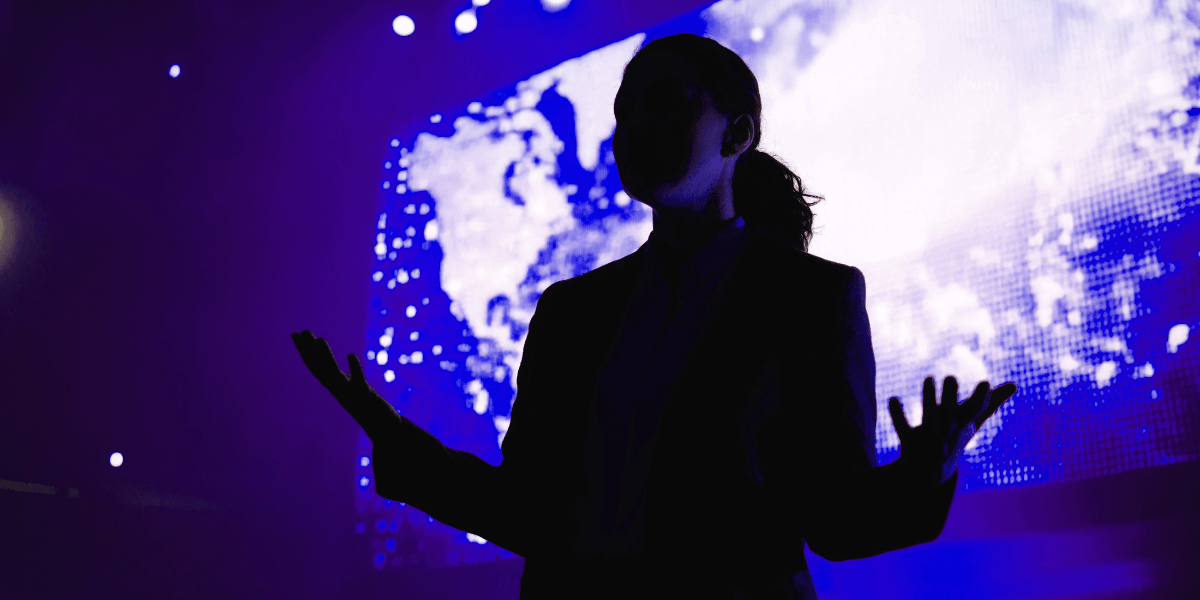 Silhouette of a businesswoman presenting on stage in front of a large digital world map display, symbolizing leadership and technology innovation.