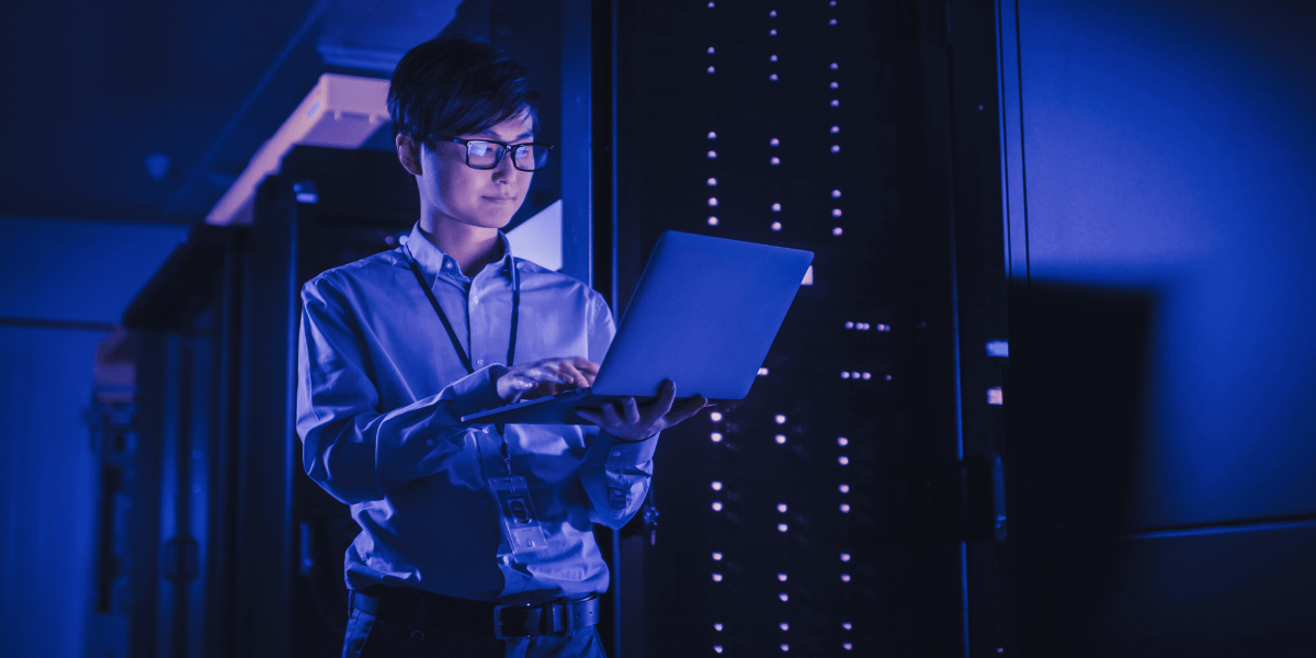 IT professional working on a laptop in a server room with glowing blue lights, symbolizing cybersecurity and data protection.