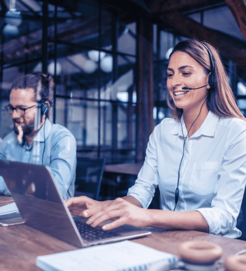 Two IT support employees working at their laptops with headsets on.